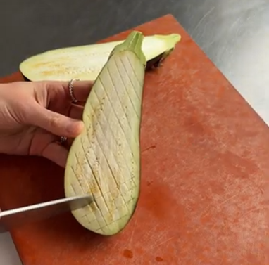 Hand holding a eggplant slice over a cutting board, with a knife at the bottom left