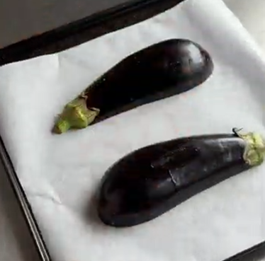 Two dark purple eggplants on a white paper towel-lined tray