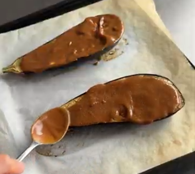 Two miso sauce-covered pastries on parchment, one being drizzled with sauce from a spoon