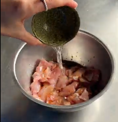 Pouring green marinade over raw chicken pieces in a metal mixing bowl