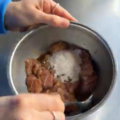 Hands holding a metal bowl of marinated meat topped with salt.