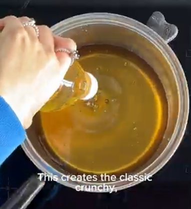 Hand pouring liquid into a pot of amber caramel on a stovetop