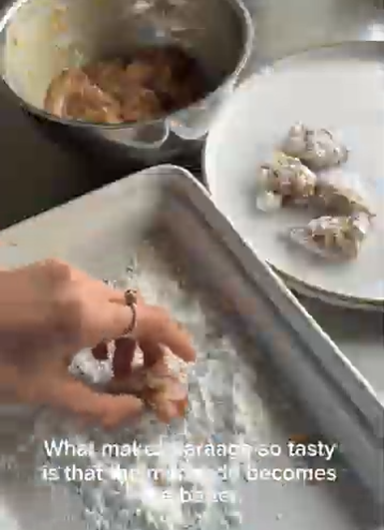 Hand mixing dough in a tray beside a metal bowl and plate of dough balls in a kitchen