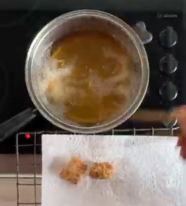 Top-down view of a pot of boiling soup on a stovetop with a paper towel holding fried bites below