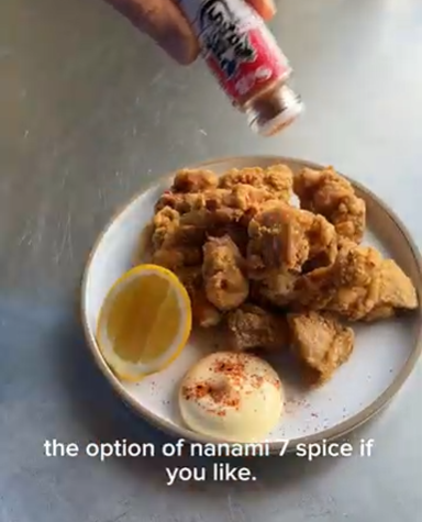 Plate of fried chicken with a dipping sauce and a hand holding a spice bottle above it.