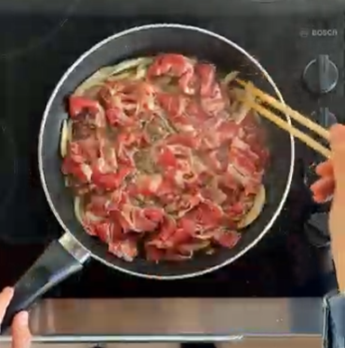 Raw meat being stirred in a pan on a stovetop with chopsticks