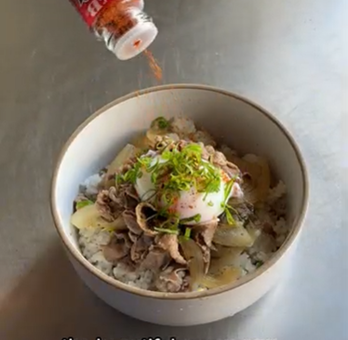 Bowl of rice topped with sliced meat, green onions, and sauce being sprinkled from above