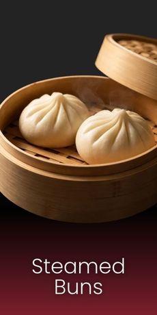 Two steamed buns rest in a bamboo steamer basket against a dark background, with text below reading