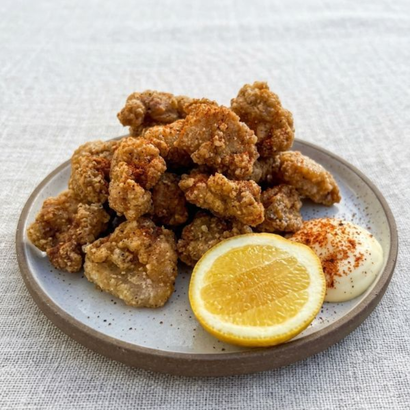Fried chicken bites on a plate with lemon wedge and dipping sauce