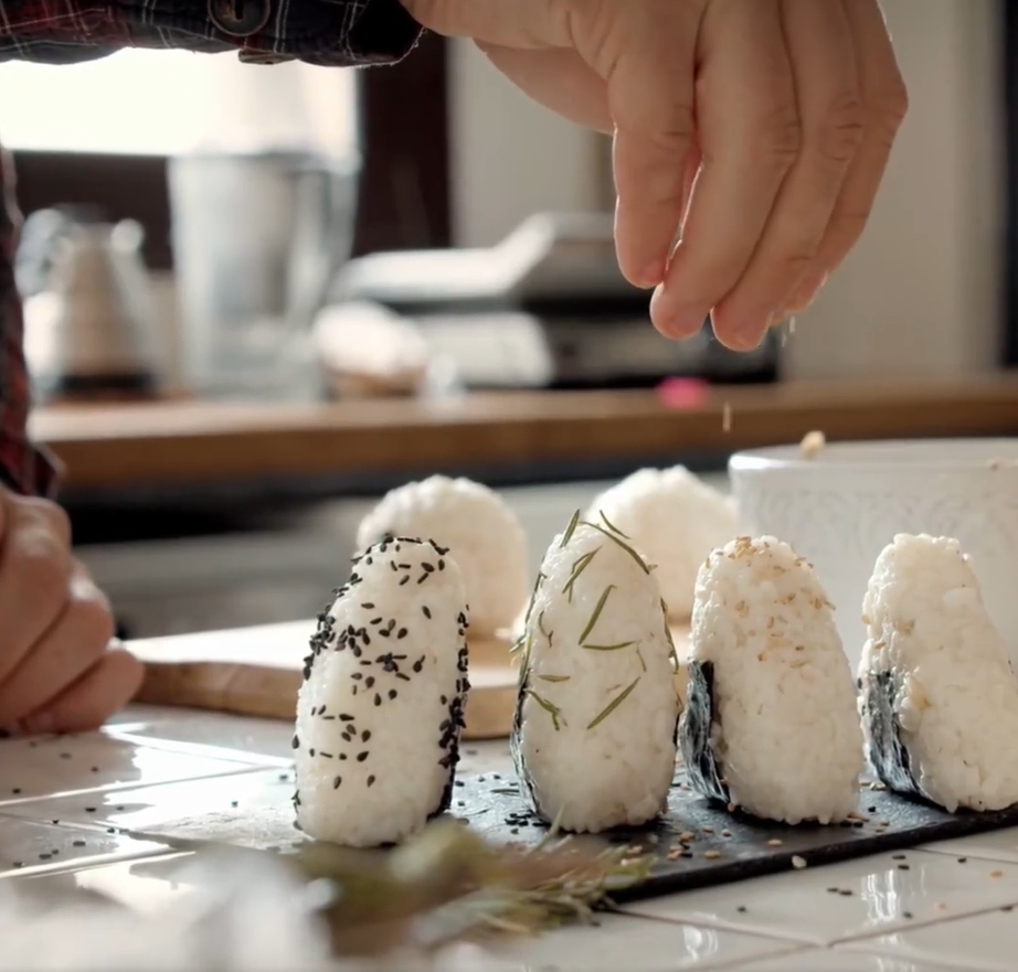 A person is preparing rice balls with sesame seeds and rosemary