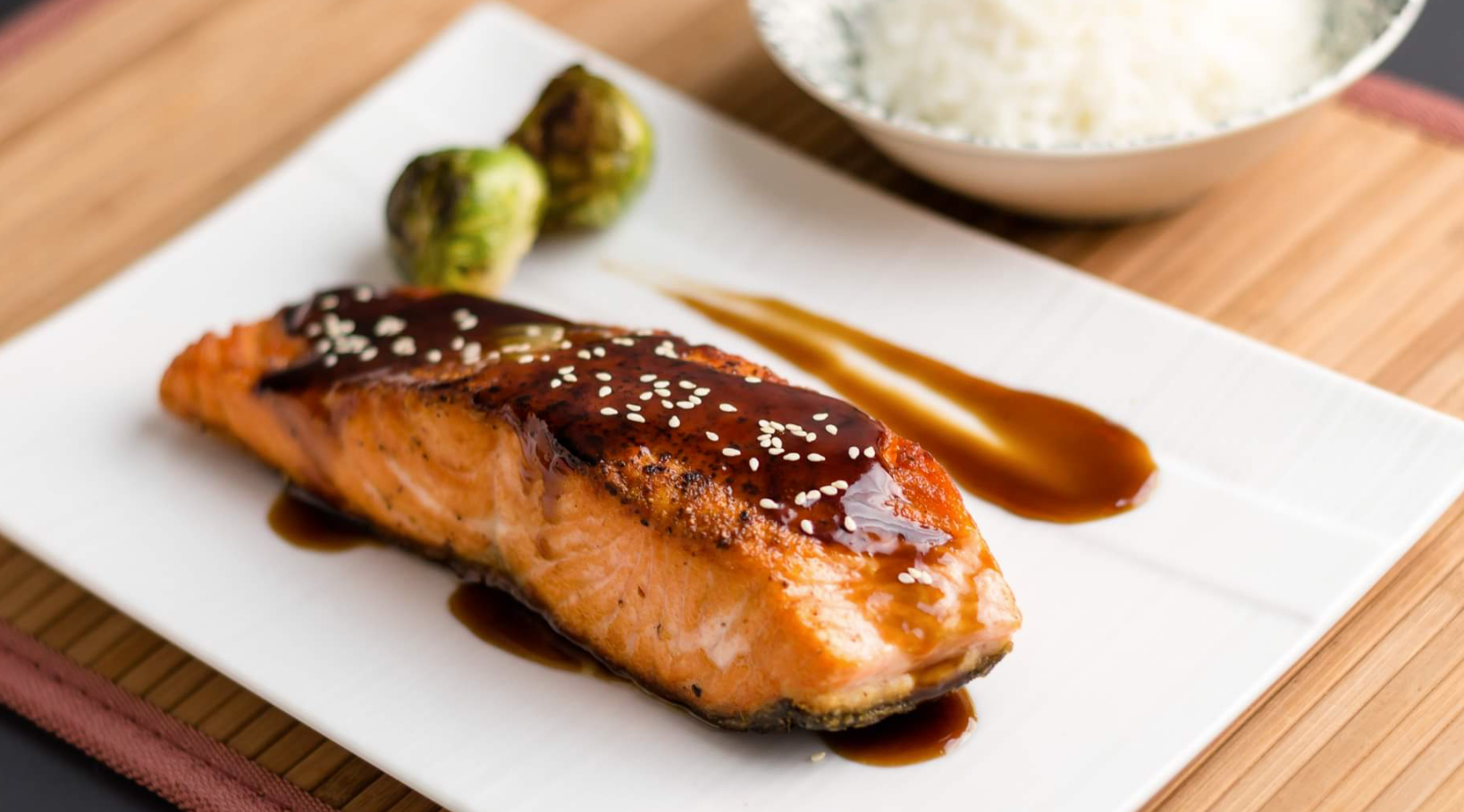Pan-seared salmon with glaze, Brussels sprouts, rice in a bowl, and sauce drizzle.