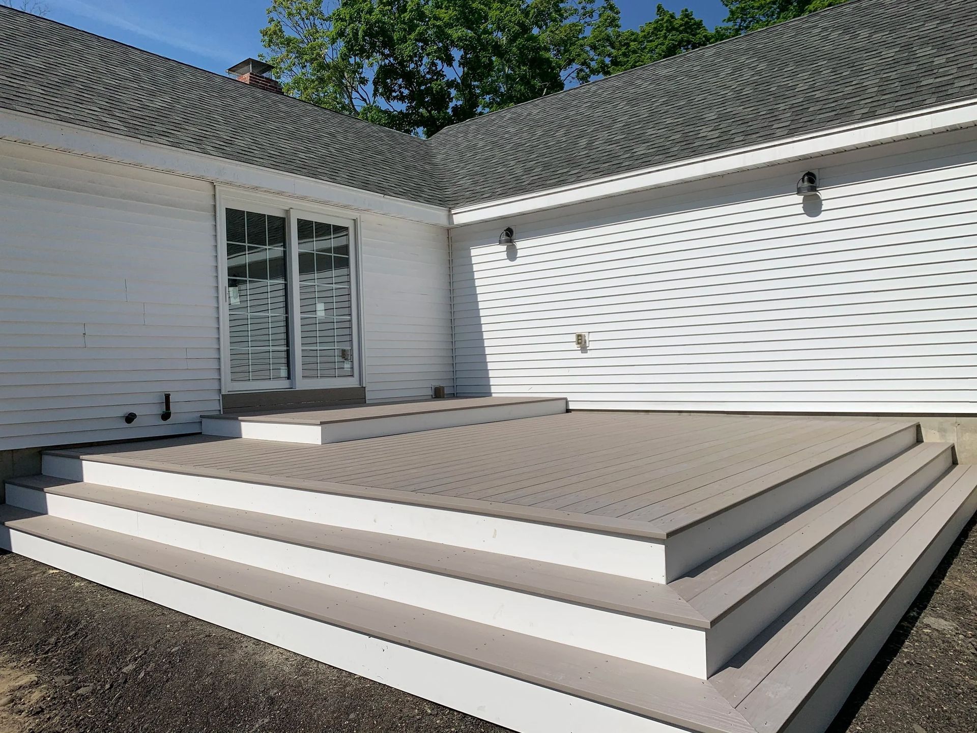 Gray composite deck with steps in front of a white house with sliding glass doors.