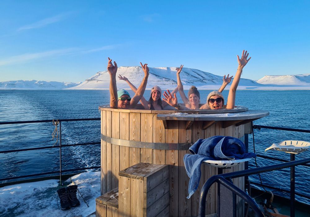 A group of people are sitting in a wooden hot tub on a boat.
