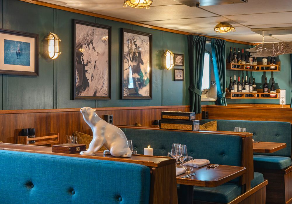 A statue of a polar bear is sitting on a bench in a restaurant.