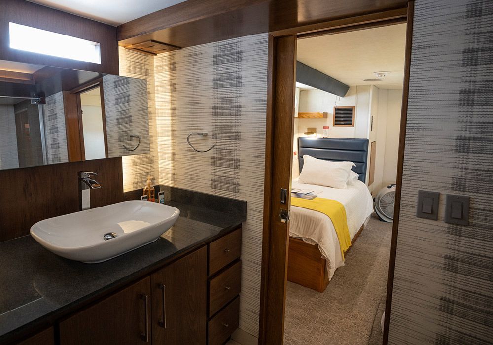 A bathroom with a sink , mirror , and door leading to a bedroom.