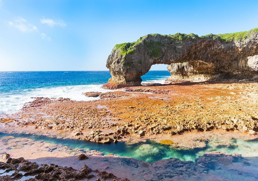 Ocean arch with turquoise water, orange rocks, and blue sky.