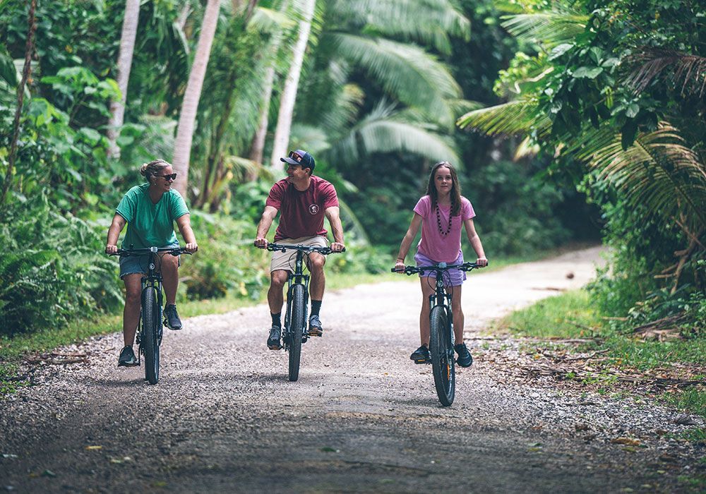 Three people biking on a gravel path through a lush, green tropical forest.