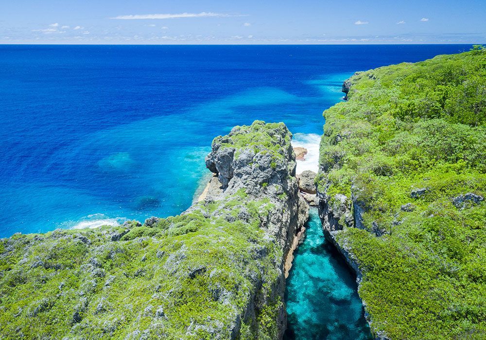 Cliffs with lush green vegetation meet the vibrant blue ocean. A turquoise channel cuts through.