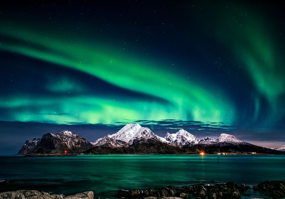 The aurora borealis is shining over the mountains and the ocean.