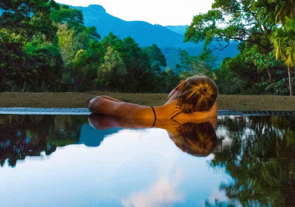 A woman is laying in a swimming pool with mountains in the background.