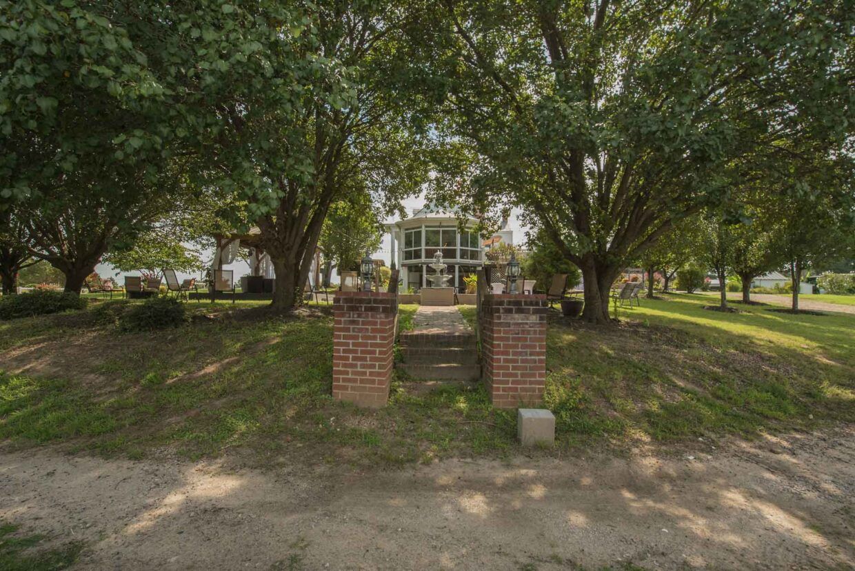 Brick stairs leading to a white house framed by two large trees. Green grass and shrubs surround the home.