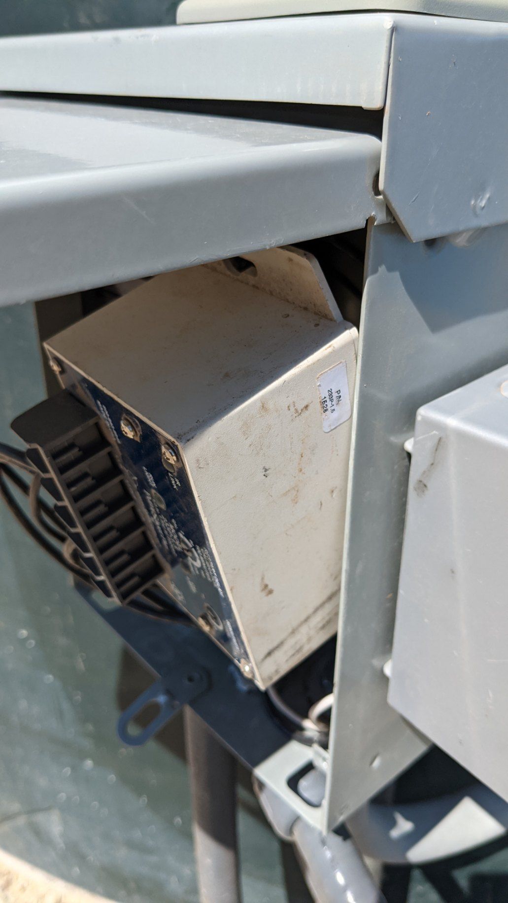 A beige, rectangular electrical device with cooling fins, mounted inside a light gray metal enclosure.