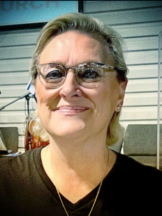 Smiling person wearing glasses in a casual indoor setting with a laptop in the background