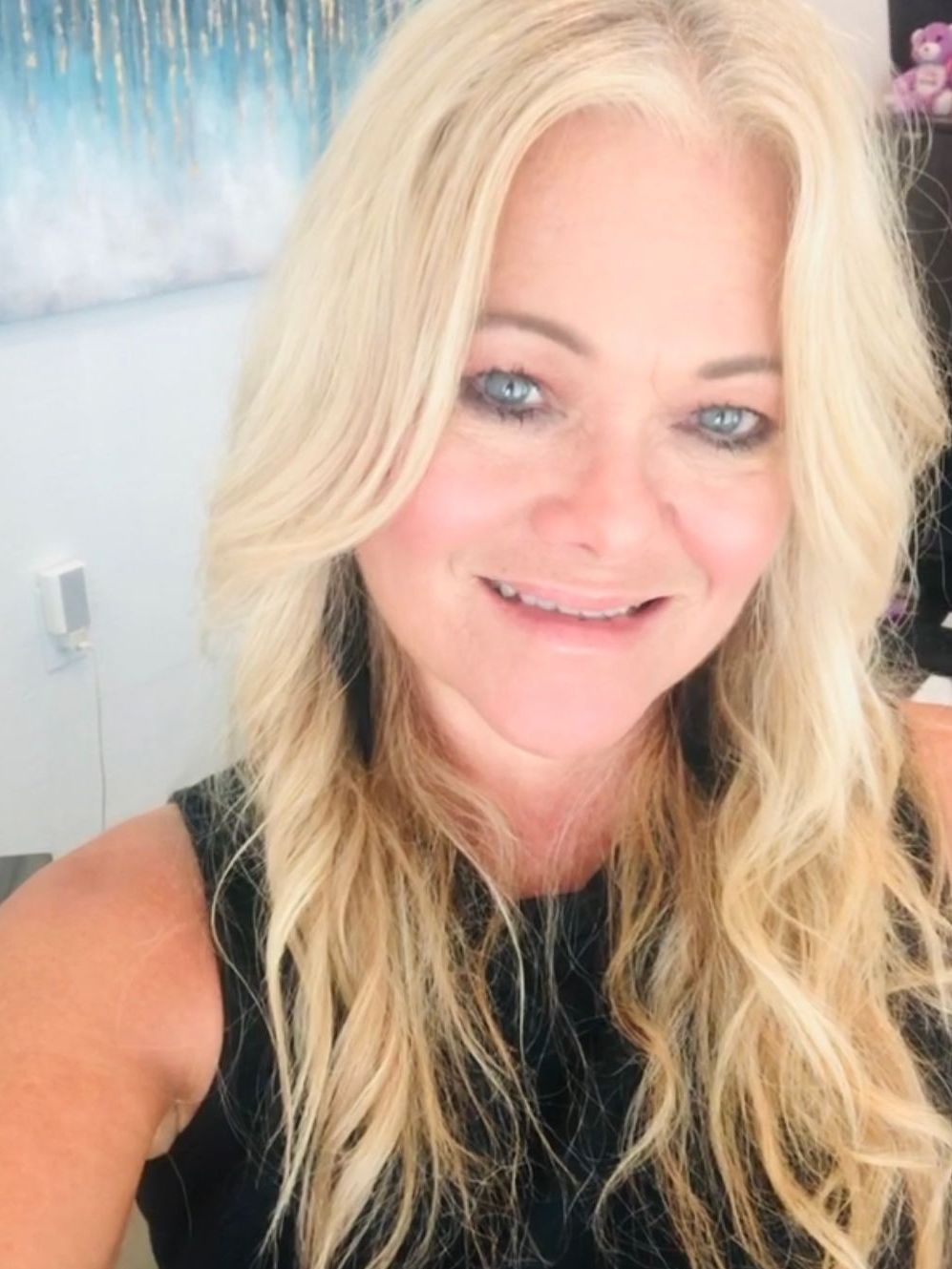 A woman with blonde hair and blue eyes is smiling for the camera.