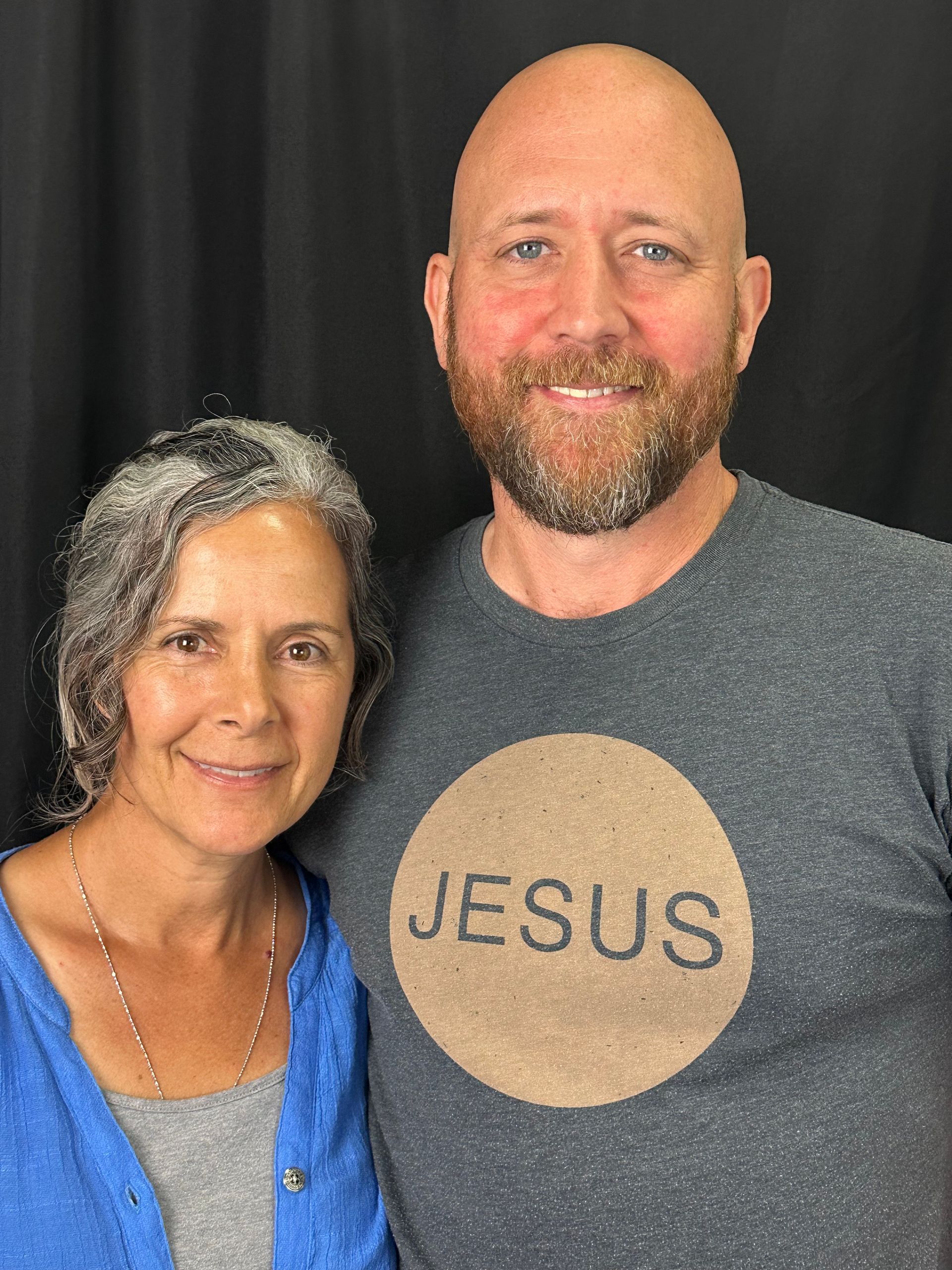 A man and a woman are posing for a picture . the man is wearing a jesus shirt.