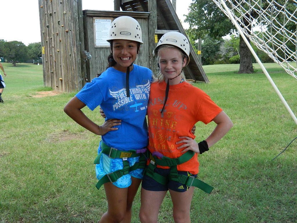 Two girls wearing helmets and harnesses pose for a picture