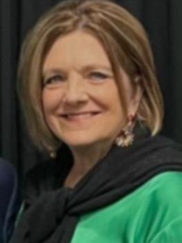A woman wearing a green shirt and a black scarf smiles for the camera