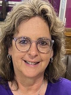 A woman wearing glasses and earrings is smiling for the camera.