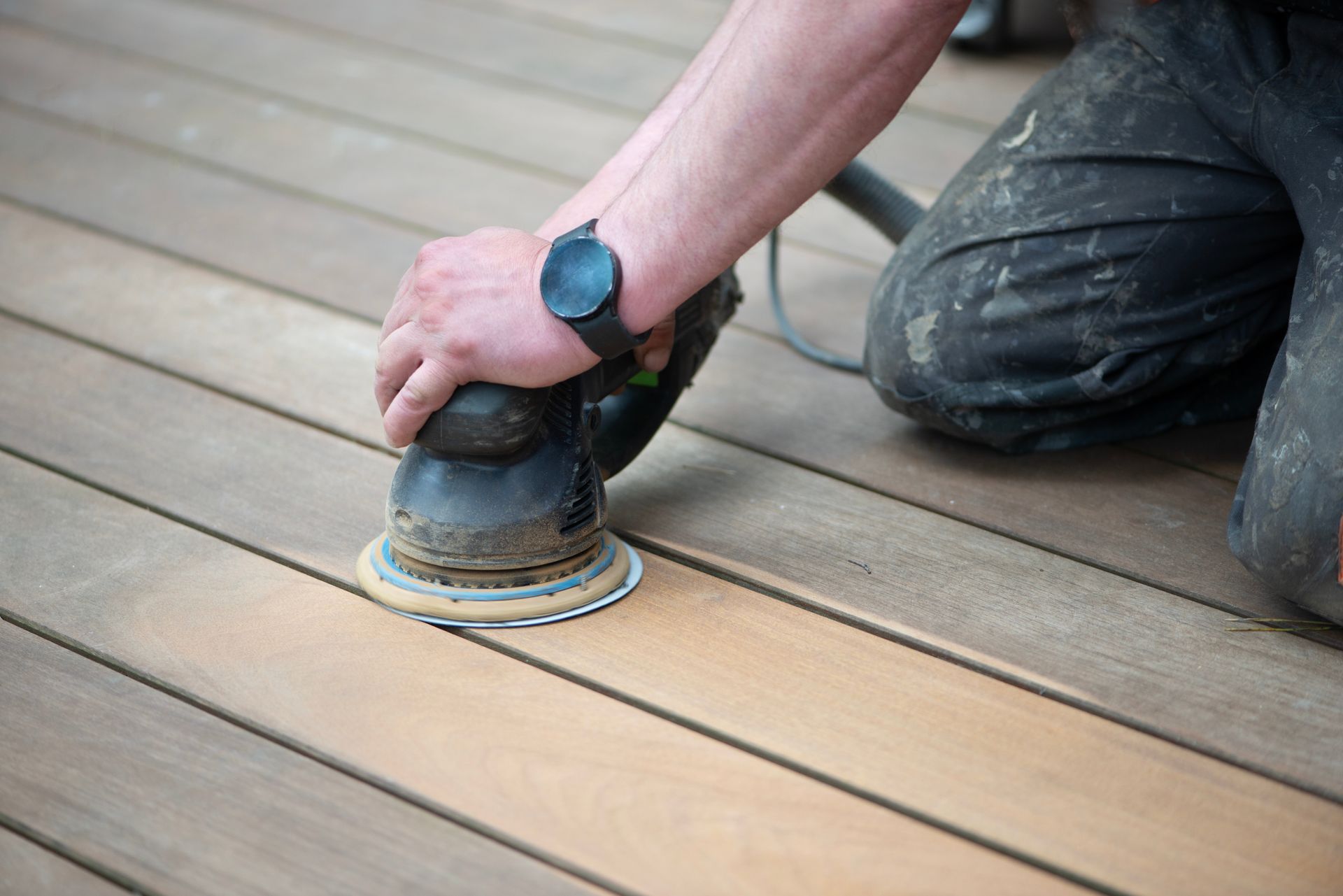 A man is sanding a wooden deck with a sander.