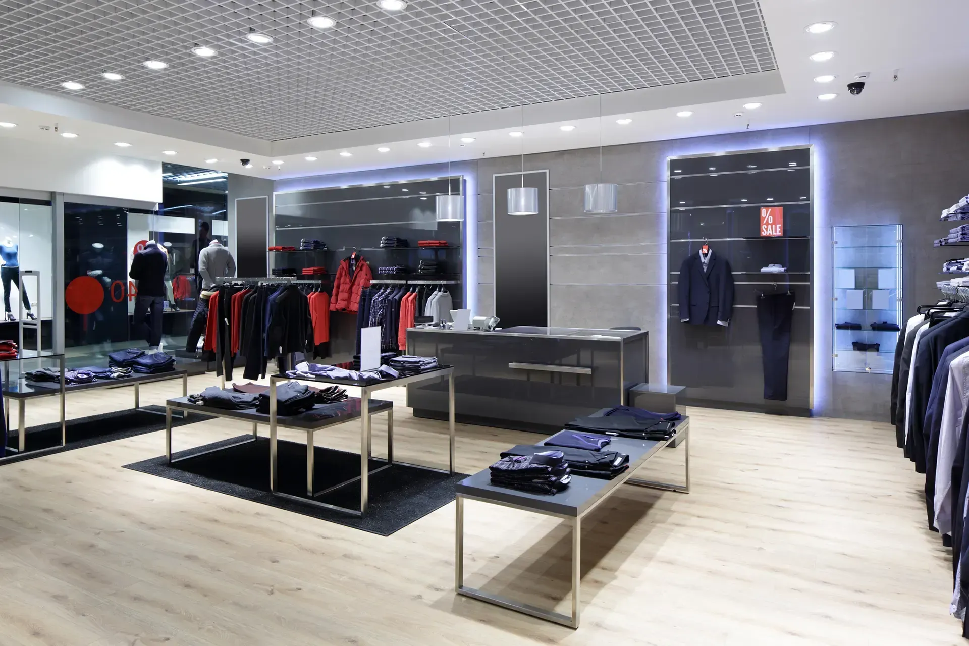 Interior of a men's clothing store with displays of jackets, shirts, and pants; neutral tones and recessed lighting.