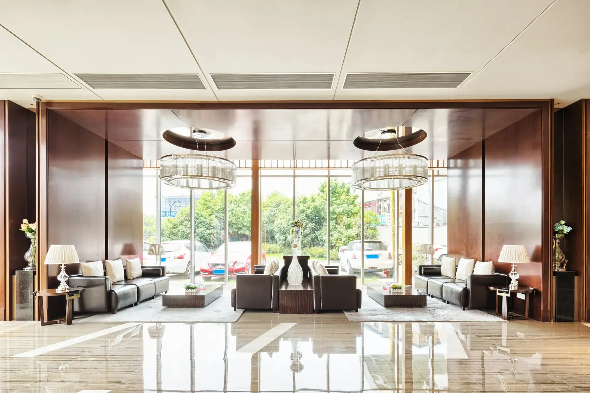 Lobby with seating and large windows. Brown wood walls, marble floor, and two large chandeliers.