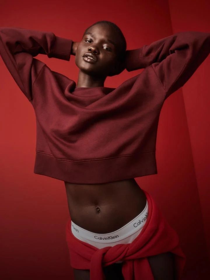 A woman is wearing a maroon sweater and calvin klein underwear with a red jacket tied around her waist.