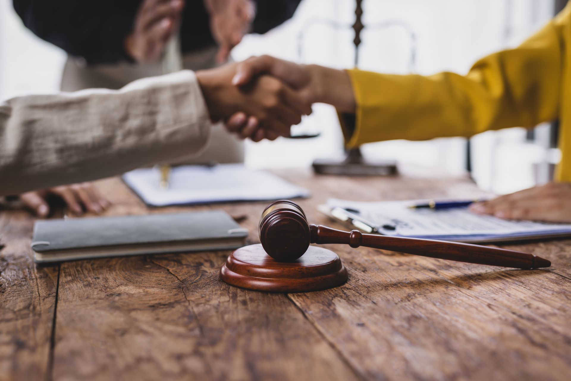 Handshake over desk with judge’s gavel and legal documents in foreground.