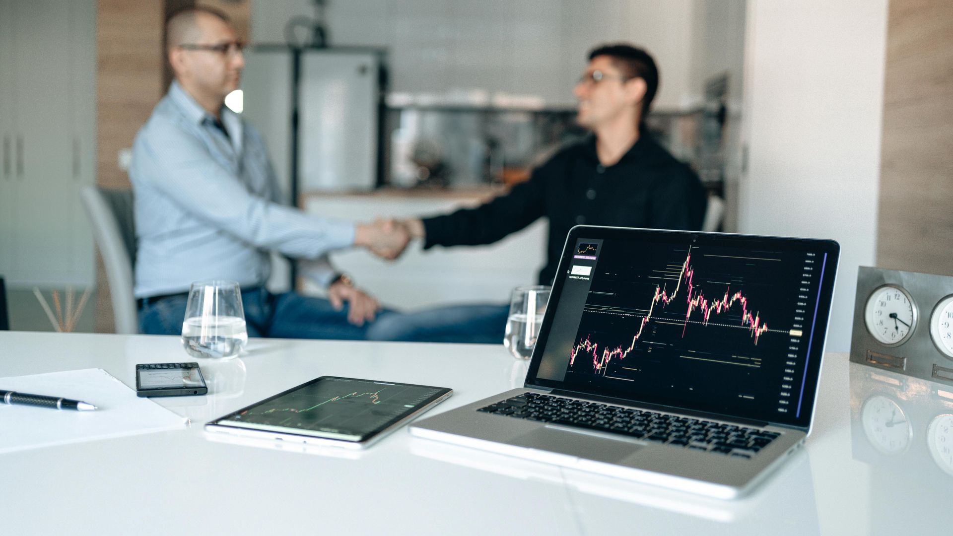 Picture of two business executives shaking hands, with a laptop in the foreground showing an investment chart