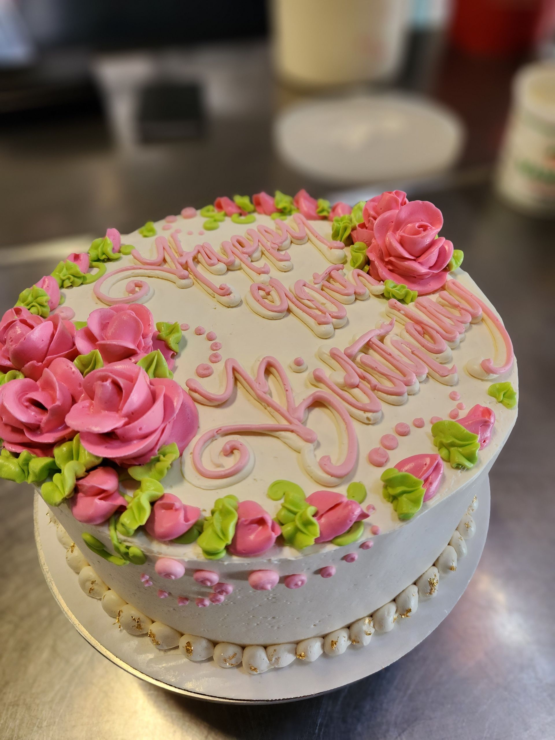 A birthday cake with pink roses and green frosting