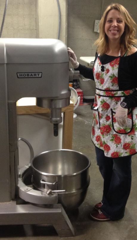 A woman in a strawberry apron is standing in front of a mixer