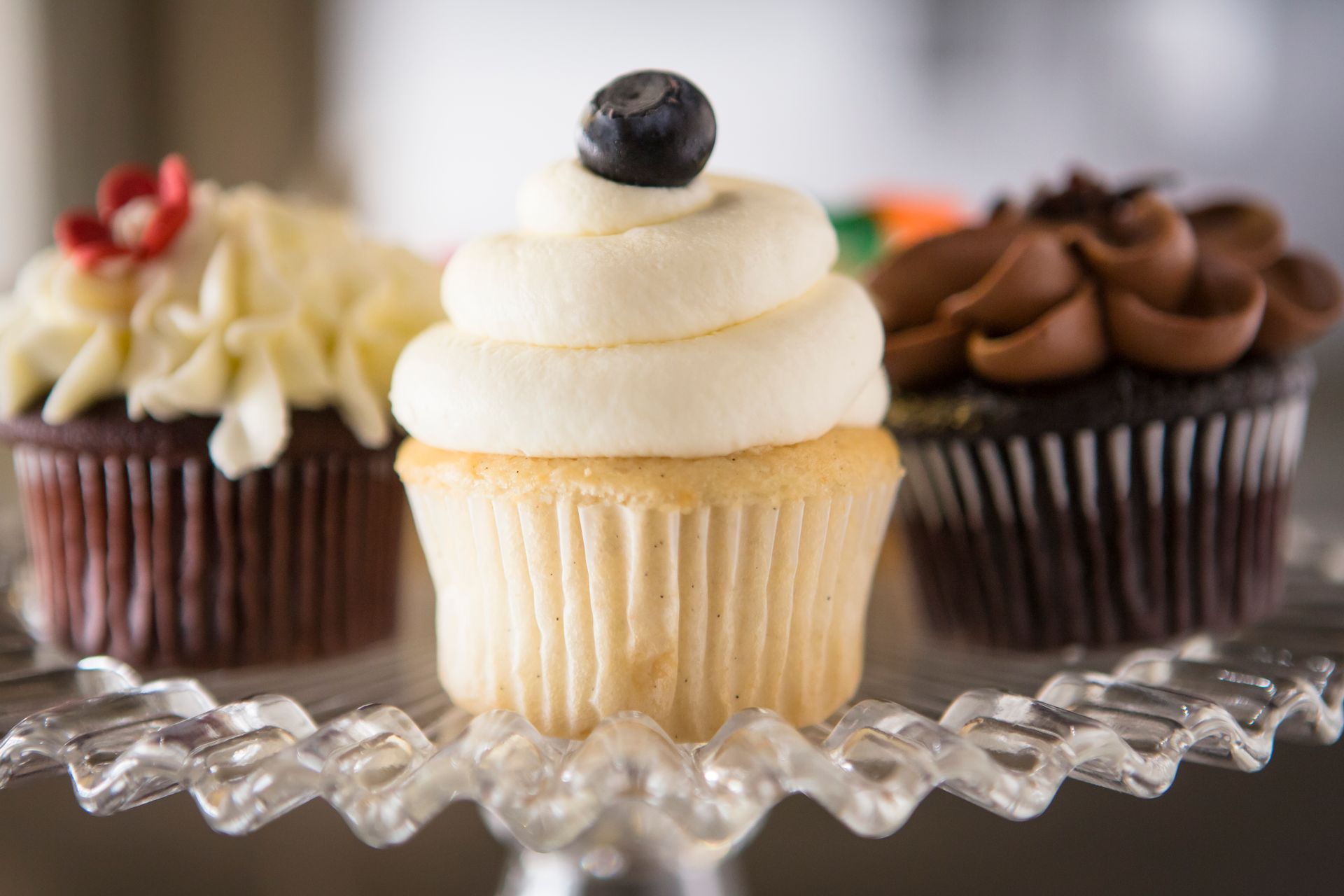 A cupcake with a blueberry on top is sitting on a glass plate next to other cupcakes.