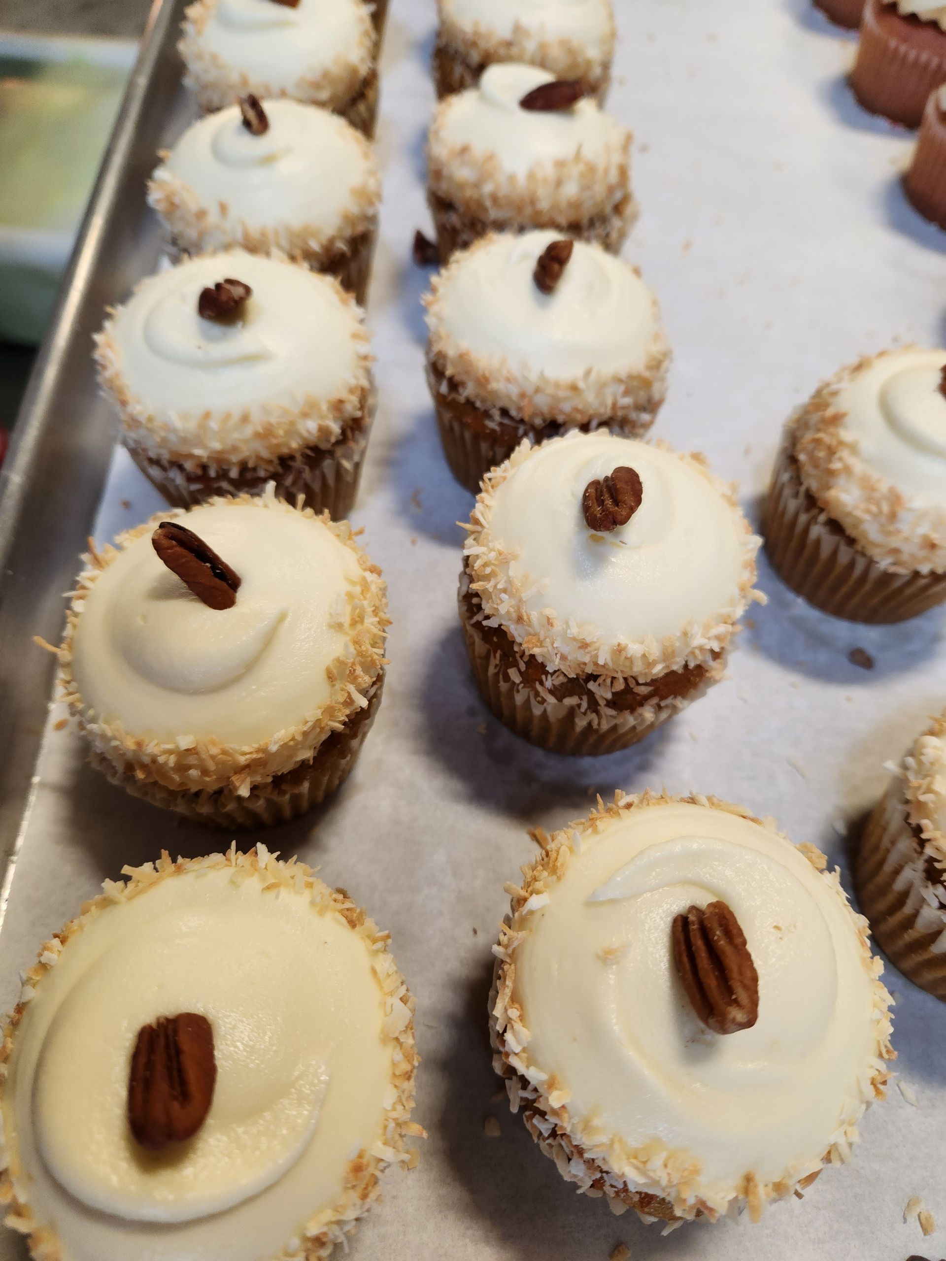 A bunch of cupcakes with white frosting and pecans on top