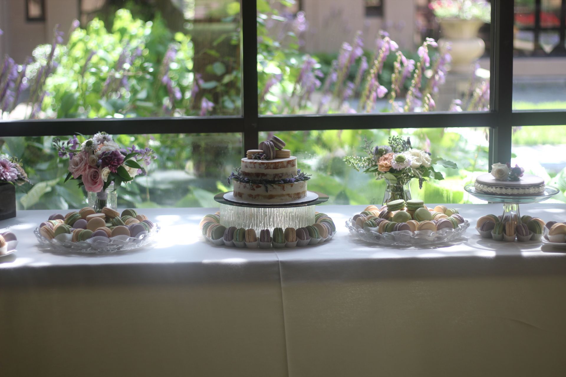 A table with a variety of desserts and cakes on it in front of a window.