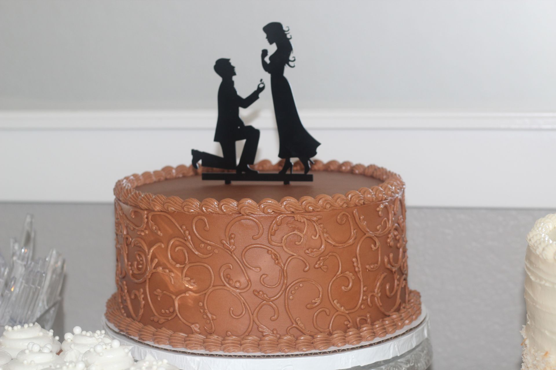 A chocolate cake with a silhouette of a man proposing to a woman on top.