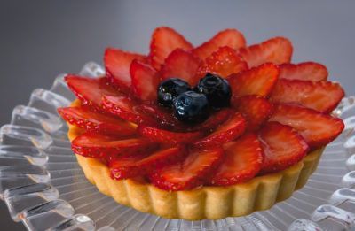 A strawberry tart with blueberries on top is on a glass plate.