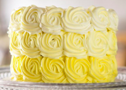 A close up of a cake with yellow frosting on a glass plate.
