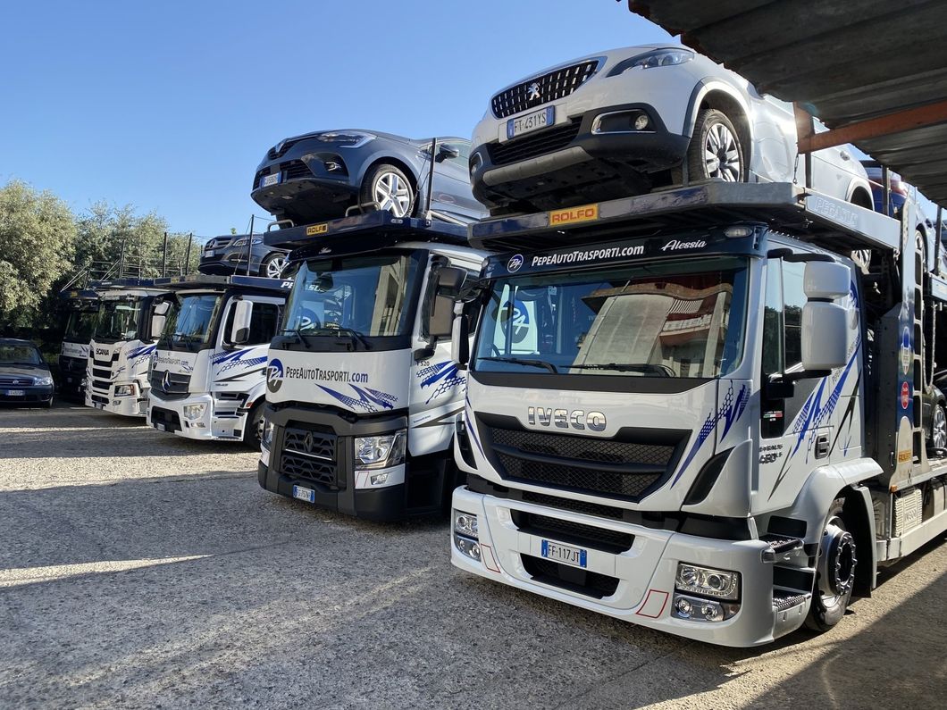 Una fila di camion con sopra delle auto sono parcheggiati in un parcheggio.