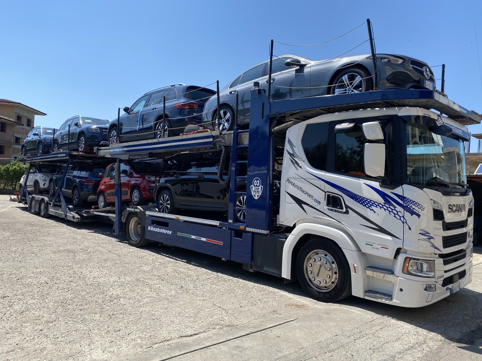 Un camion che trasporta automobili è parcheggiato in uno spiazzo ghiaioso.