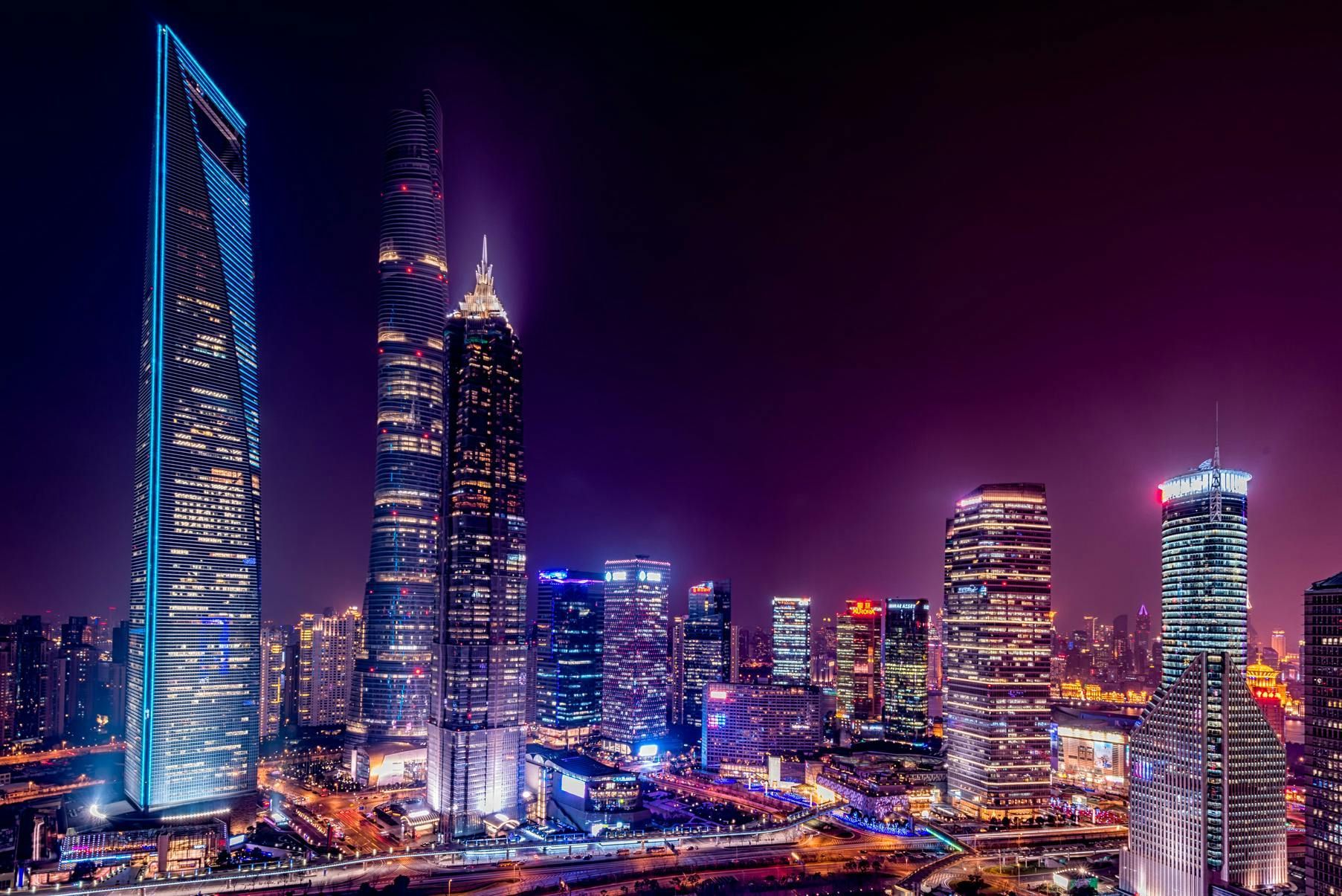Night view of Shanghai skyline with illuminated skyscrapers against a purple sky.