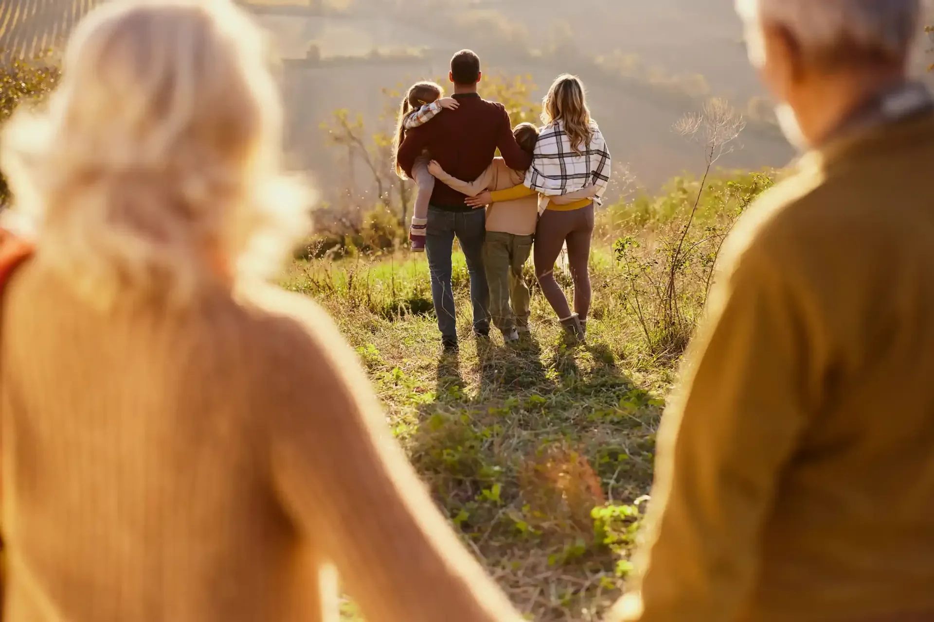 Family walking in sunlight; grandparents in the foreground, younger family in the background enjoying outdoors.